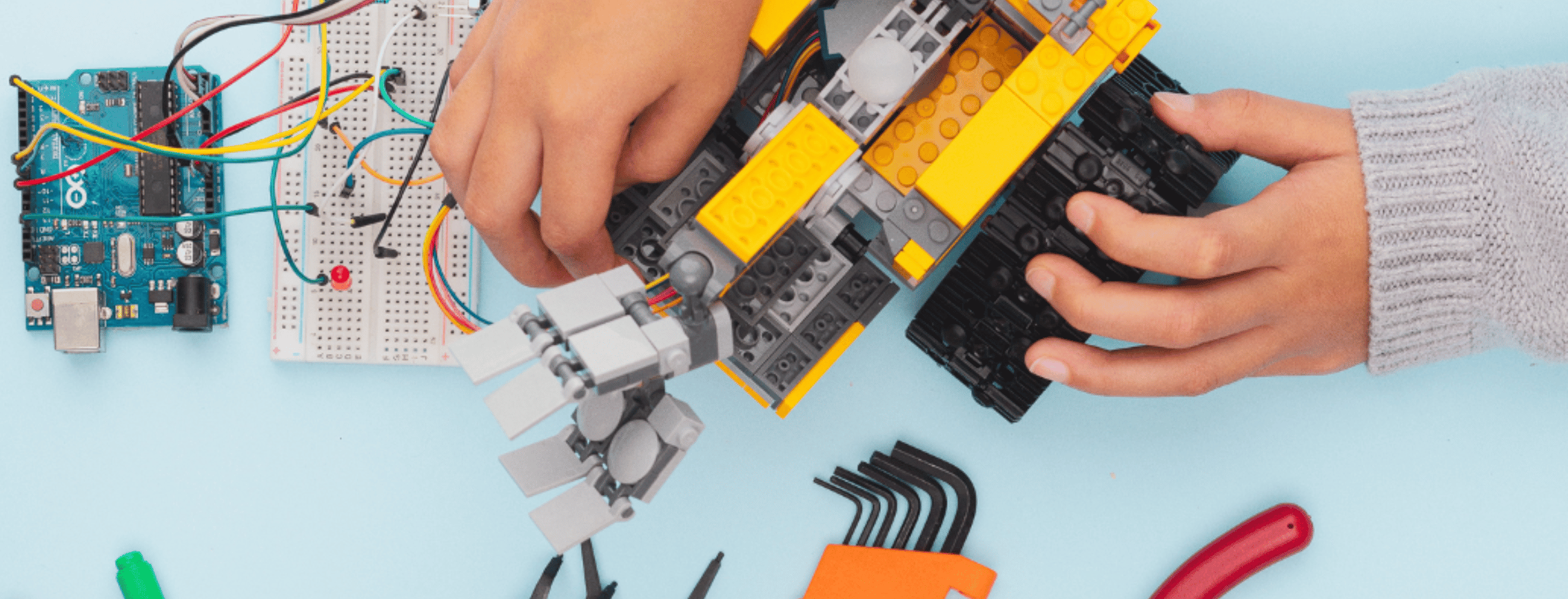 Close-up of a child assembling a robotic arm using circuit boards and wires during a hands-on robotics class.