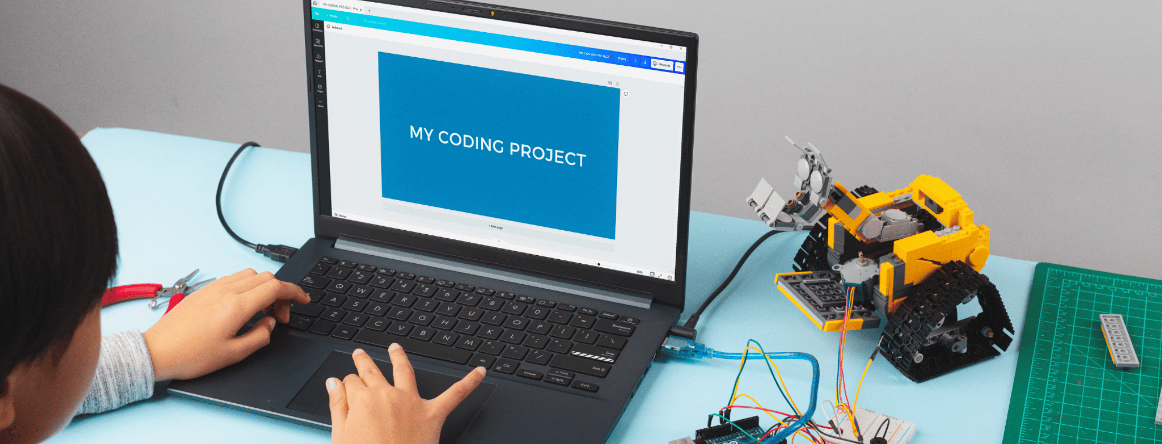 Child working on a coding project on a laptop, with a robotic arm and tools on the desk.